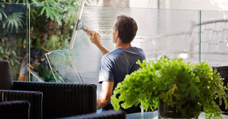 Cleaners - Man in Gray Shirt Cleaning Clear Glass Wall Near Sofa